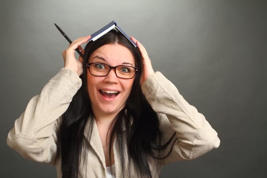 the girl, the brunette wearing spectacles with a notebook on the head, on a gray background, looks in the chamber, panics, a double 2