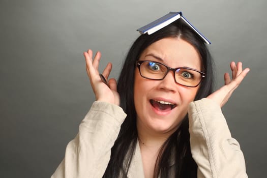 the girl, the brunette wearing spectacles with a notebook on the head, on a gray background, looks in the chamber, panics