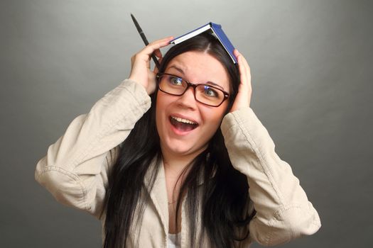 the girl, the brunette wearing spectacles with a notebook on the head, on a gray background, looks in the chamber, panics, a double 3