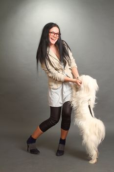 The beautiful brunette wearing spectacles with a white shaggy doggie on a gray background