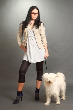 The beautiful serious brunette wearing spectacles with a white shaggy doggie on a gray background