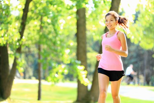 Runner - woman running in city park on sunny summer day with with sunshine in green trees. Asian / Caucasian fitness sports model during outdoor workout.
