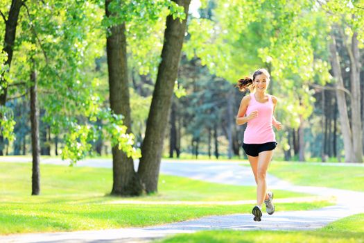 Jogging woman running in park in sunshine on beautiful summer day. Sport fitness model of mixed Asian / Caucasian ethnicity training outdoor for marathon.