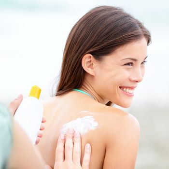 Sunscreen lotion on beach. Couple applying sunscreen lotion. Woman smiling happy on summer vacation. Mixed race Caucasian / Asian Chinese young woman.