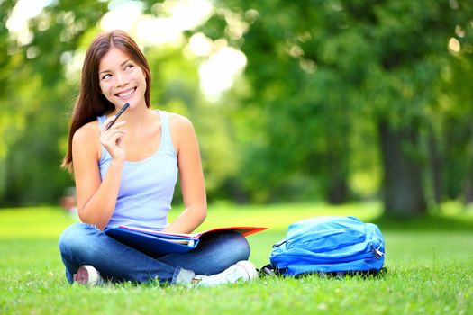 Student thinking looking in park Joyful happy asian girl student sitting writing and reading outside on university campus or park. Mixed race Chinese Asian / Caucasian female student woman looking at camera.