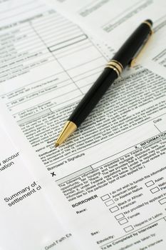 Vertical orientation of blank loan documents spread out with a pen pointing to where the borrower will sign