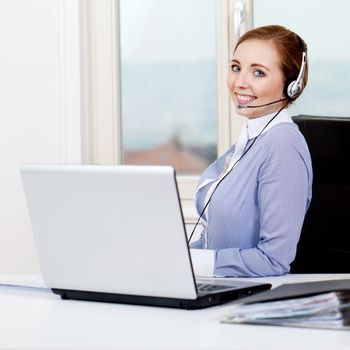 smiling young female callcenter agent with headset in office