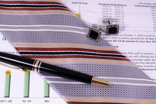 A pen, tie, and cufflinks on top of investment literature