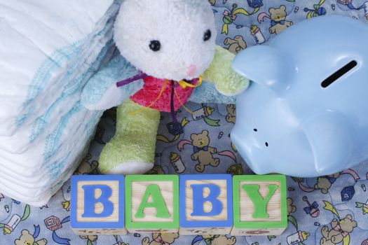 Wooden blocks spell baby, blue piggy bank, bunny toy, and diapers sit on a baby blanket