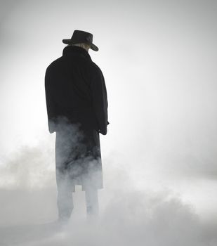 standing woman with dark coat and flowing fog around her feet