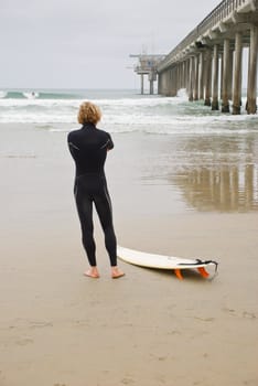 A vertical shot of a single surfer preparing to enter the water next to a pier
