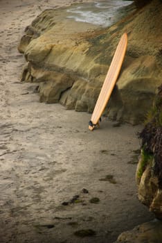 A single surfboard stands against colorful rocks in the stand