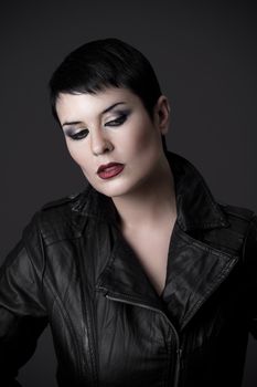 Sexy young brunette woman in leather jacket over dark background