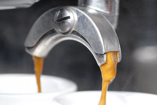 A shot of coffee pouring into two espresso cups. Focus on near portafilter spout.