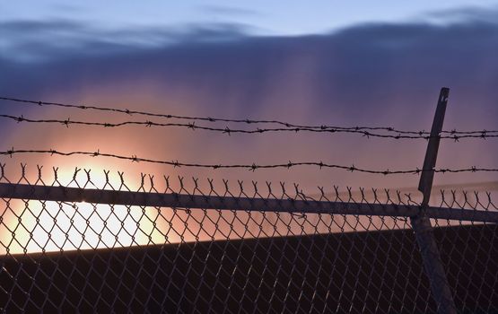 A barb wire fence with sunset in yellow, orange, purple and blue.