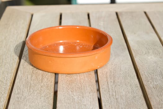 An earthenware bowl shaped ashtray on a table top made of hard wood slats.