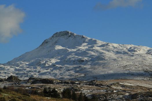 The snow covered peak of Yr Aran, Snowdonia National park, Wales, UK, against a blue sky with cloud.