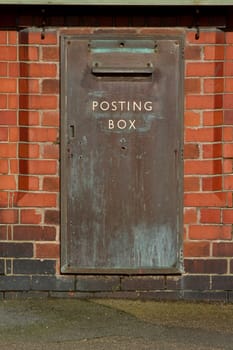 A vintage large metal post box built into a red brick wall with the words 'posting box' written on it.