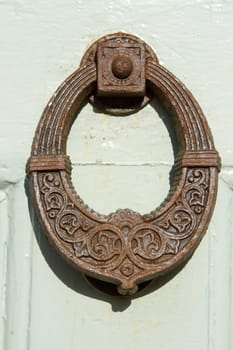 A vintage rusty metal door knocker with ornate markings on a wooden white painted door.