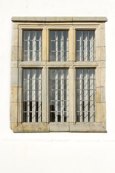 An historic window frame carved from sandstone and assembled in parts against a white painted wall.