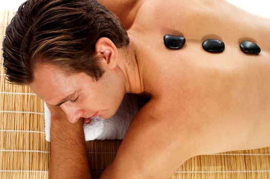 Man relaxing on massage bed with hot stones isolated over white background