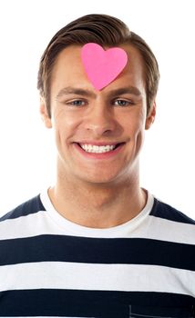 Attractive man posing with pink paper heart on his forehead