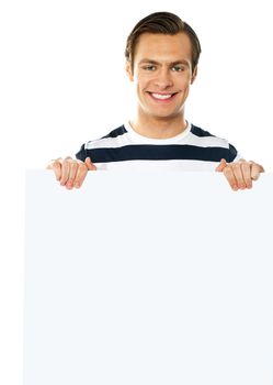 Casual young man holding a blank poster against white background