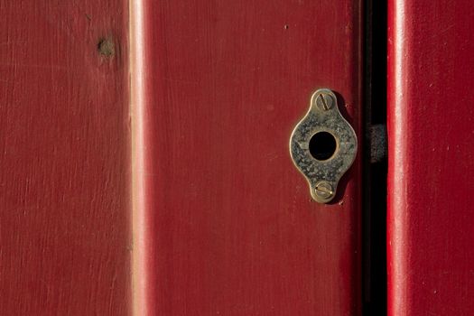 A vintage brass dead lock screwed to a red gloss painted door with the bolt showing in the gap.