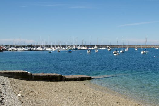 A set of concrete steps leads into the clear waters of a marina with moored yachts and a breakwater in the background.