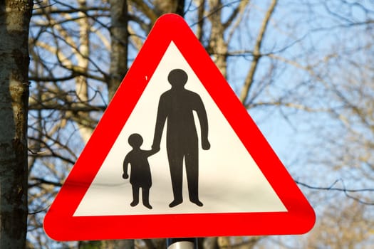 A caution sign with an adult and child in black on a white background with a red triangular border.