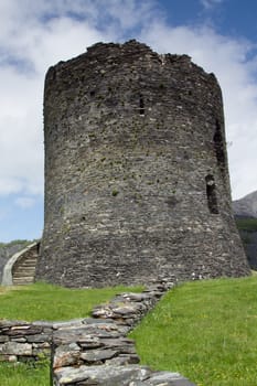 A low wall flanked by grass leads to a stone built tower with a set of steps against a blue sky with clouds.