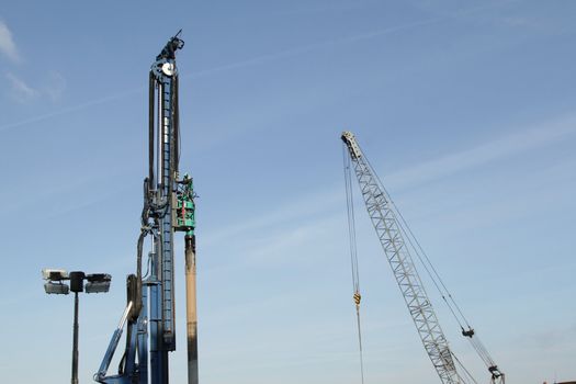 A blue painted pile driver and a crane set against a blue sky.