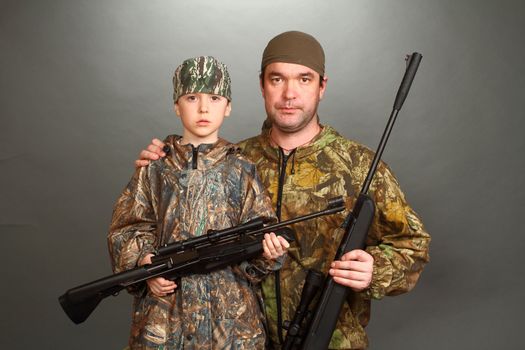 the boy and the adult man in a camouflage with rifles nearby in a shot, a look in a chamber lens