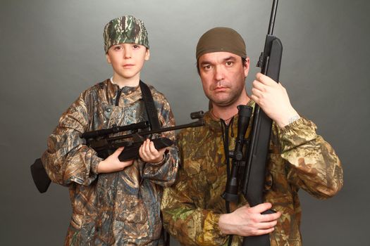 the boy and the adult man in a camouflage with rifles nearby in a shot, look in the chamber