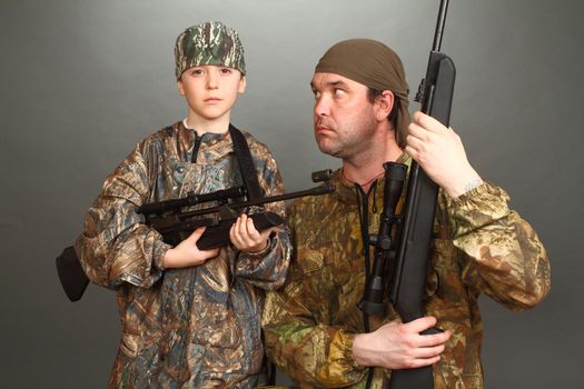 the boy and the adult man in a camouflage with rifles nearby in a shot