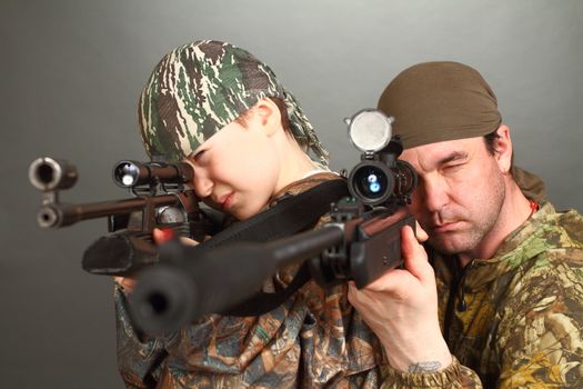 the boy and the adult man in a camouflage with rifles aim