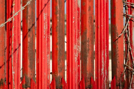 A background of metal vertical sections painted red with areas of rust and flaking paint with barbed wire as a frame.