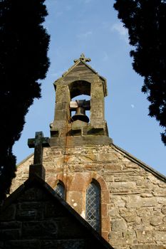 Looking through silhouette trees and a shaded cross to a church bell tower with a bright blue sky behind.