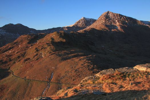 The East side of the Snowdon Massif in the dawn light with the miners track visible and the peaks of Crib Goch and Snowdon against a blue sky, Snowdonia National Park, Wales, UK.