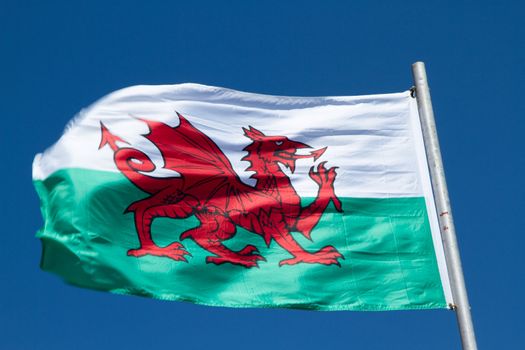 Welsh flag with a red dragon on green and white flutters in the wind against a blue sky.