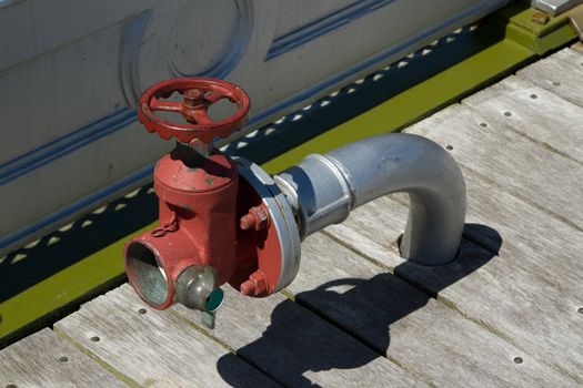 A fire hydrant pipe emerges from wooden decking with a red connector and tap handle.