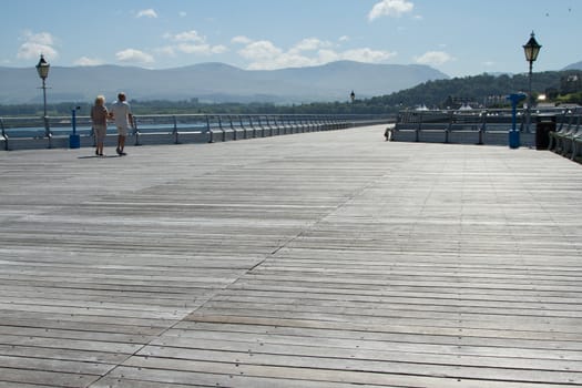 A couple walks arm in arm along the board walk of a pier.