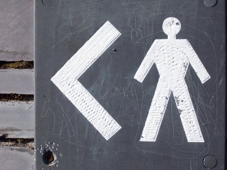 A grey slate plaque with the symbol of a man and left pointing arrow painted in white.