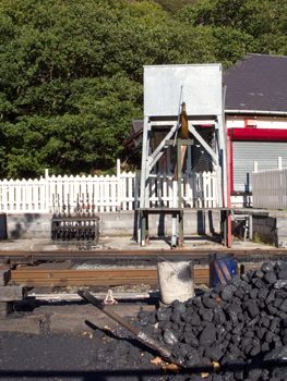 A steam train railway line with a water tank and a pile ot coal with a shovel and buckets.