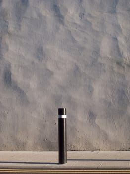 A painted uneven rendered wall with a slab pavement and post and double yellow lines in front.