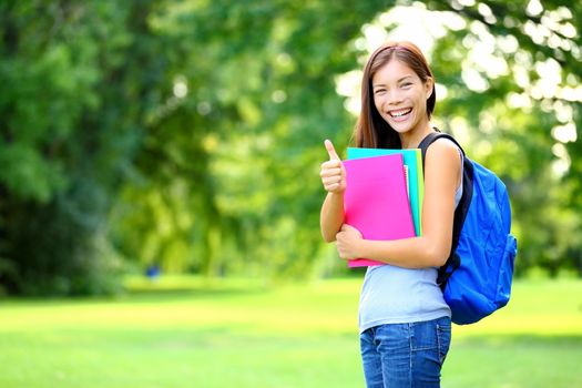 Student in park showing happy thumbs up success sign. Mixed race Asian Caucasian woman university student holding books outside.