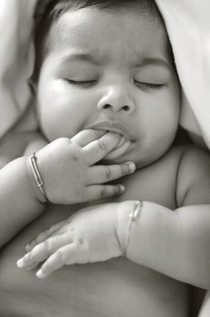 6 months old Asian Indian baby girl sucking her fingers when sleeping, black and white