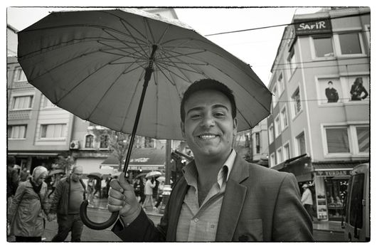 BIG SMILE IN THE RAIN, ISTANBUL, TURKEY, APRIL 14, 2012: Young man with umbrella sending a big smile to the photographer, Istanbul, Turkey.