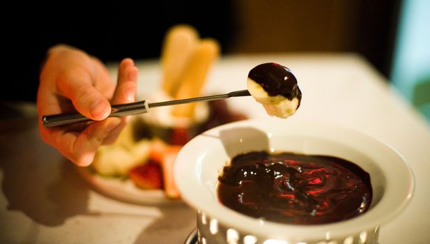 Banana coated in chocolate fondue on a fondue fork