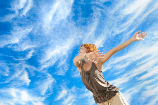 Beautiful young dancer performing yoga-dance outdoors with blue sky and clouds in the background